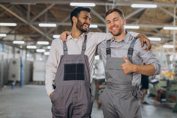 Two happy international workers in overalls hug each other against a factory background