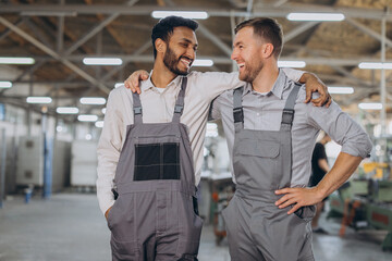 Two happy international workers in overalls hug each other against a factory background