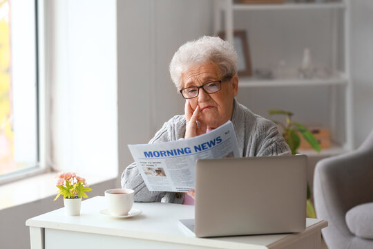 Senior woman reading newspaper at home