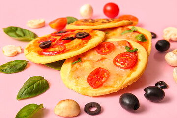 Different tasty mini pizzas and ingredients on pink background