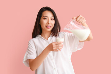 Beautiful Asian woman pouring milk into glass on pink background