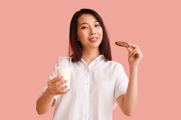 Young Asian woman with milk and cookie on pink background