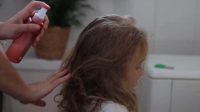 A woman helps to get rid of lice and parasites on the head of a little girl, combs her head with a special comb. Treatment of lice and nits