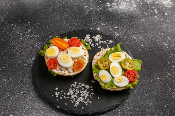 Rice crackers with quail eggs, tomatoes and lettuce on dark grunge background