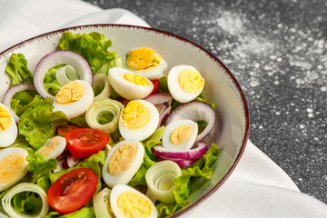 Tasty salad with quail eggs, tomatoes, onion and lettuce on dark grunge background, closeup