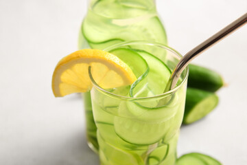 Glass and bottle of infused water with cucumber slices on white background