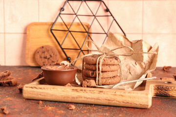 Wooden tray with cookies, chocolate cream and spoon on brown grunge table near tile wall