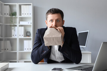 Young businessman with paper bag having panic attack in office