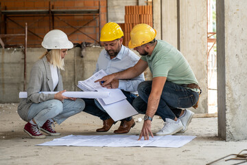 A female architect and a focused construction managers engage in an animated discussion, analyzing blueprints. - 615609681