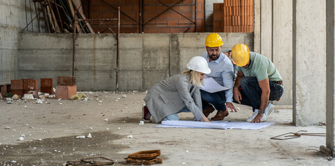A female architect and a focused construction managers engage in an animated discussion, analyzing blueprints.