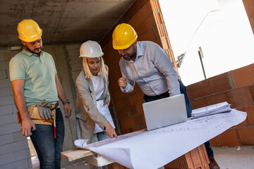 A female architect and a focused construction managers engage in an animated discussion, analyzing blueprints.