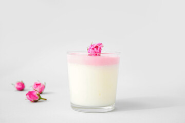 Glass of panna cotta with beautiful pink rose flowers on lilac background