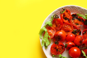 Plate with tasty grilled tomatoes and arugula on yellow background