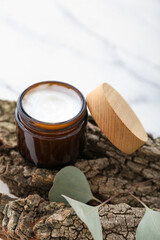 Tree bark with jar of cream and eucalyptus twig on grunge white background