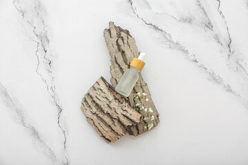 Bottle of cosmetic oil with flowers and tree bark on grunge white background