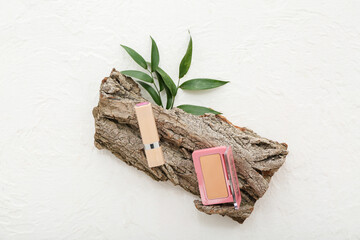 Powder with lipstick, leaves and tree bark on grunge white background