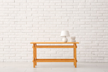 Wooden table with lamp and decorative figure near white brick wall