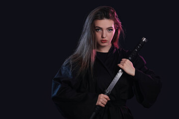 Beautiful young woman with katana on dark background