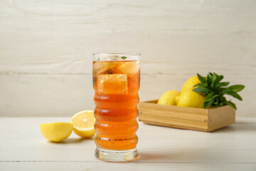 Glass of ice tea and box with lemons on white wooden background