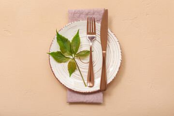 Beautiful table setting with clean plate, cutlery and green plant leaves on beige background