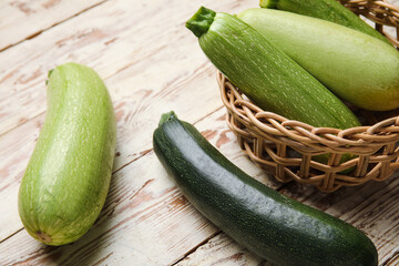 Wicker bowl with fresh green zucchini on white wooden background