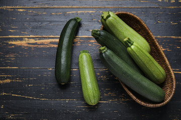 Wicker bowl with fresh green zucchini on black wooden background