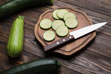 Board with slices of fresh green zucchini on wooden background