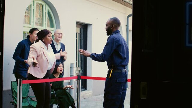 Shoppers Arguing With Security Officer, Waiting For Black Friday Seasonal Sales Outside Clothing Store. Crazy Anxious Mall Clients Feeling Tired Of Waiting In Line At Shopping Center.