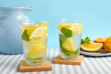 Glasses and jug of infused water with lemon and mint on blue background