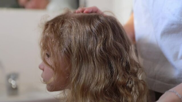 A woman helps to get rid of lice and parasites on the head of a little girl, combs her head with a special comb. Treatment of lice and nits