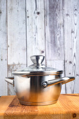 Stainless steel saucepan with a glass lid on a wooden table. Side view.