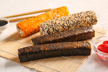 Tasty sushi rolls and bamboo mat on light background