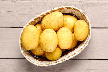 Wicker bowl with raw baby potatoes on grey wooden background