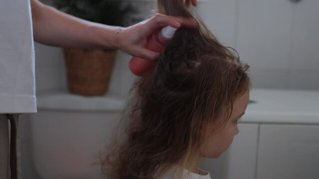 A woman helps to get rid of lice and parasites on the head of a little girl, combs her head with a special comb. Treatment of lice and nits