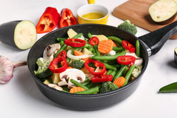 Frying pan with fresh vegetables on light background