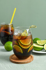 Glasses of cold Cuba Libre cocktail and plate with limes on grey background