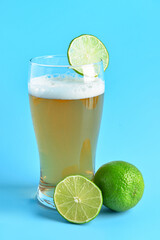 Glass of cold beer with lime on blue background