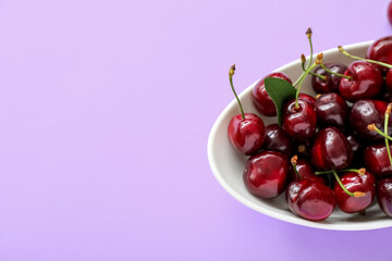 Bowl with sweet cherries on lilac background
