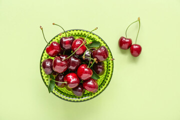 Bowl with sweet cherries on green background