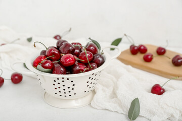 Colander and board with sweet cherries on white background