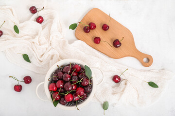 Colander and board with sweet cherries on white background