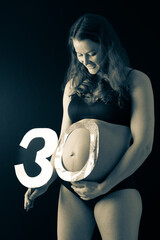 Baby bump shot with glittering lion sticker and 30 birthday shield from the side of smiling...