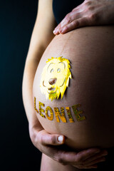 Baby bump shot with glittering lion sticker and child name from the side of pregnant woman at home....