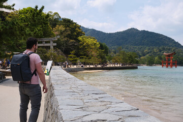 European tourist visiting Itsukushima Jinja Otorii or Grand Torii Gate on the sea of Miyajima,...