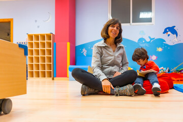 Portrait of a female teacher with a child sitting reading a story book, indoor of a kindergarten