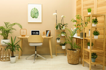 Stylish workplace with laptop, armchair and houseplants in room. Interior design