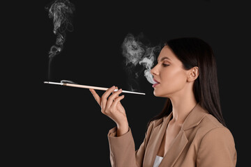 Fototapeta premium Woman using long cigarette holder for smoking on black background