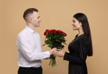 Boyfriend presenting beautiful bouquet roses to his girlfriend on beige background. Valentine's day celebration