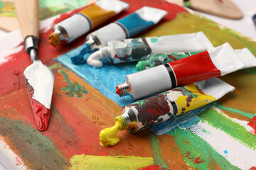 Tubes of colorful oil paints and spatula on canvas with abstract painting, closeup