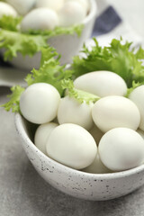 Peeled boiled quail eggs in bowl on grey table, closeup